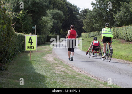 Rollstuhl Athleten mit Zyklus Marschall und Frau runner Pass 4 km Zeichen Stockfoto