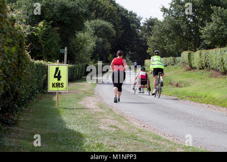 Rollstuhl Athleten mit Zyklus Marschall und Frau runner Pass 4 km Zeichen Stockfoto