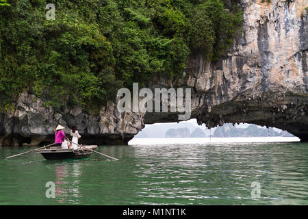 Junge Frauen auf einem Ruderboot außerhalb einer Höhle in der Halong Bay, Vietnam posieren. Die kleinen Inseln und Kalkfelsen Formationen haben sich von der UNESCO zum geschützten Bereich. Stockfoto