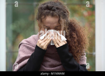 Outdoor Portrait einer Frau, die ihre Nase weht in Papier Gewebe Stockfoto