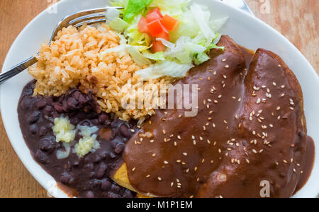 Chicken Enchiladas Mole Poblano, mit schwarzen Bohnen, brauner Reis und Salat Stockfoto