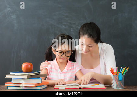 Lächelnde junge Mutter Lehre schöne hübsche Vorschule Mädchen studieren in Schwarzes Brett Hintergrund, wenn kleine Tochter bereit zurück zu Schule educatio akzeptieren Stockfoto