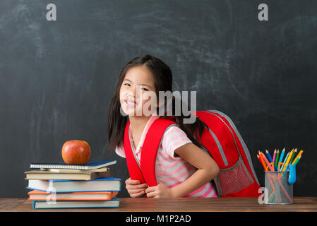 Junge schöne Mädchen Schüler, die Schultasche Gefühl schwer im Schwarzen Brett Hintergrund und Gesicht zur Kamera, unglücklich Emotion. Stockfoto