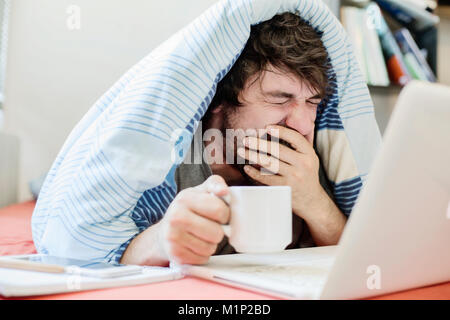 Junger Mann lernt, gähnt, während der Computer im Bett, Home Office, Deutschland Stockfoto