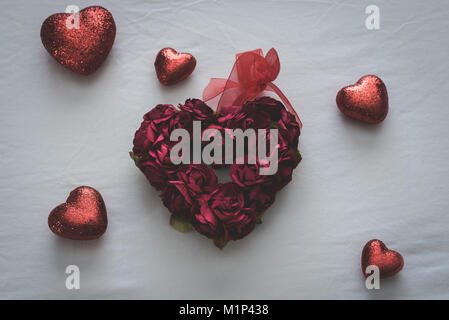 Herzform aus kleinen Rosen mit kleineren Herzen auf einem weißen Bettlaken umgeben. Stockfoto