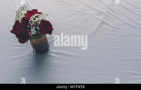 Blick von oben auf die Rosen in einer Vase auf einem weißen Bettlaken für Hintergrund und Text Raum auf der rechten Seite. Stockfoto