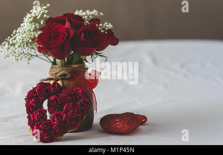 Rosen in einer Vase mit anderen Herzen auf einem weißen Bett angezeigt. Verlassen text Raum auf der rechten Seite. Stockfoto