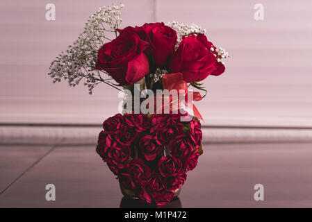 Rosen in einer Vase mit einem Herzen aus mehreren kleineren Rosen davor posieren. Stockfoto