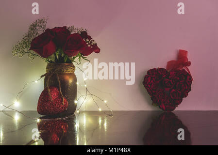 Vase mit Rosen Herz vor es bedeckt mit verdrahteten Scheinwerfern und direkt neben einem Herzen aus mehreren Rosen. Stockfoto