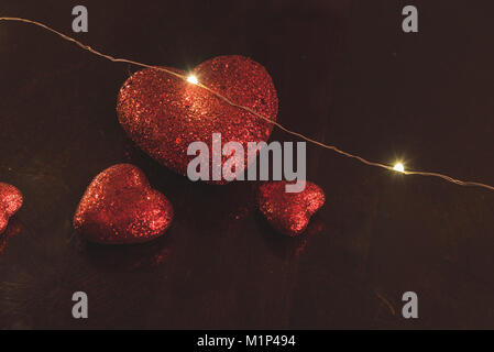 Große rote Herzen mit anderen kleineren roten Herzen auf einen Holztisch mit einem einzigen Kabel Licht auf es. Stockfoto