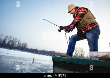 Reifen Fischer zieht Fisch aus gefrorenem Wasser eingehängt Stockfoto