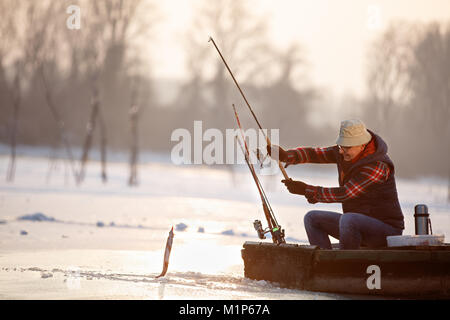 Reifen Fischer zieht Fisch aus Wasser angespannt auf dem Winter Stockfoto