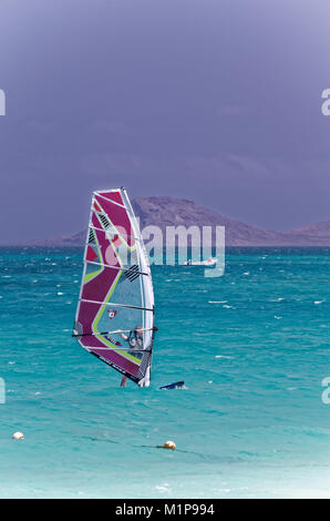 Windsurfer Mann an Bord mit roten Segeln am Meer an einem sonnigen Tag auf und blauer Himmel. Freizeit Wasser Sport während idyllische Sommer Urlaub. Stockfoto