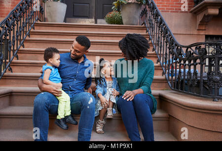 Junge Familie mit Kindern sitzt auf der vorderen Stoops Stockfoto