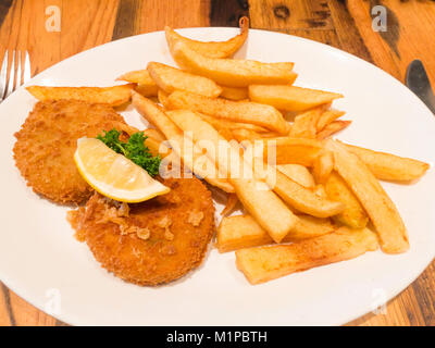 Ein Café das Mittagessen von geräuchertem Schellfisch Fischfrikadellen mit Pommes frites einer Scheibe Zitrone und Petersilie garnieren Stockfoto