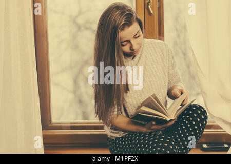 Ein nettes Mädchen ist mit einem Buch sitzen auf der Fensterbank. Angenehmen Zeitvertreib. Stockfoto