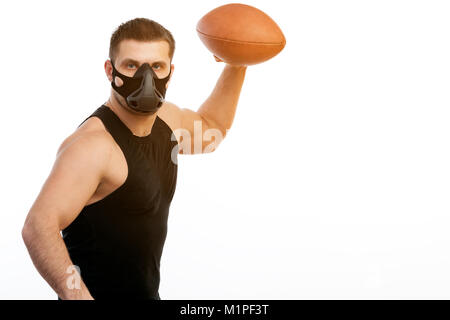 Eine junge sportliche blauäugigen Mann in ein sportliches schwarzes T-Shirt und eine schwarze Maske training hält einen Rugby Ball auf einem weißen Hintergrund isoliert Stockfoto