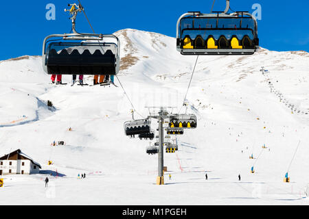 Skifahrer gehen Auf dem Sessellift gegen strahlend blauen Himmel - Ski Resort in Italien an sonnigen Wintertag Stockfoto