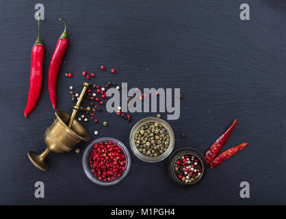 Verschiedene Pfeffer und Paprika und Pfeffer Mühle am Schwarzen Stein Hintergrund, Ansicht von oben, kopieren Raum Stockfoto