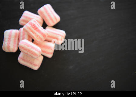 Essen von Süßigkeiten Zucker überzogen behandelt oder Süßigkeiten in Pastelltönen und Streifenmuster auf schwarzem Schiefer Hintergrund mit Platz Stockfoto