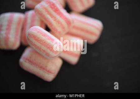 Essen von Süßigkeiten Zucker überzogen behandelt oder Süßigkeiten in Pastelltönen und Streifenmuster auf schwarzem Schiefer Hintergrund mit Platz Stockfoto