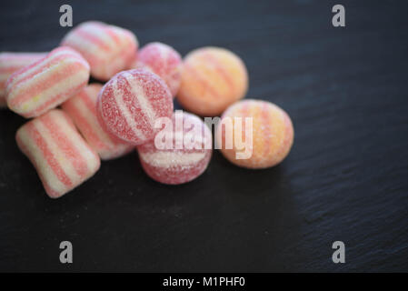 Essen von Süßigkeiten Zucker überzogen behandelt oder Süßigkeiten in Pastelltönen und Streifenmuster auf schwarzem Schiefer Hintergrund mit Platz Stockfoto