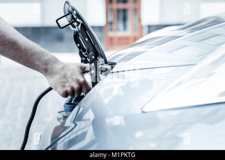 Nahaufnahme der männlichen Hand Elektroauto aufladen Düse Stockfoto