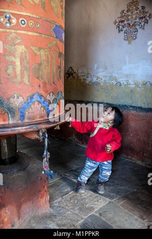 Bumthang, Bhutan. Little Boy ziehen große Gebetsmühle, jambay Lhakhang Kloster. Stockfoto