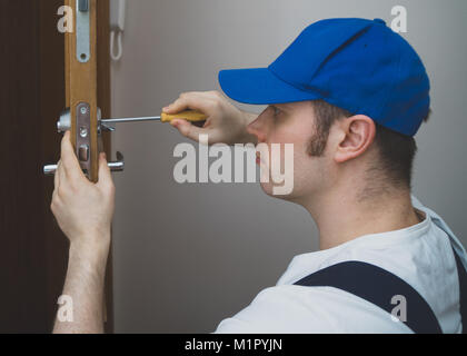 Junge Handwerker in Uniform ändern Türschloss. Stockfoto