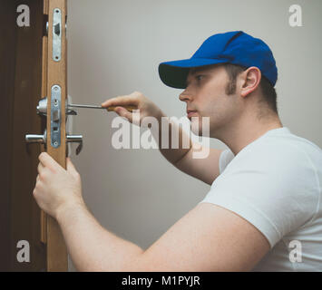 Junge Handwerker in Uniform ändern Türschloss. Stockfoto