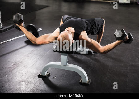 Junger Mann tun Hantel auf der Bank in der Turnhalle Fliegen Stockfoto