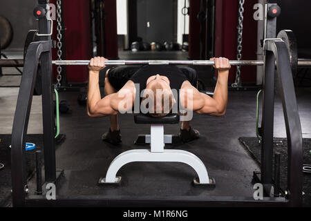 Junger Mann lag auf der Bank drücken Sie während des Trainings mit Barbell In der Turnhalle Stockfoto