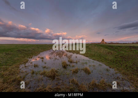 Dramatische rosa Wolken kurz vor Sonnenuntergang an der isolierten hl. Thomas Becket Kirche im Fairfield auf Romney Marsh, Kent, Großbritannien. Stockfoto