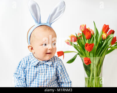 Niedliches Kleinkind sitzt neben Vase mit Tulpen Stockfoto