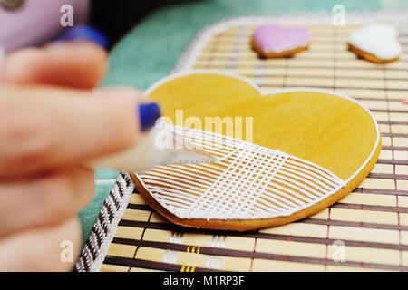 Frau Konditor schmückt und schmückt die Glasur mit Lebkuchen Kekse in der Form des Herzens. Stockfoto