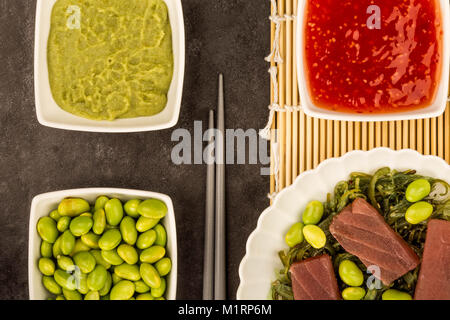 Im japanischen Stil rohen Thunfisch Sashimi auf einem Bett von eingelegtem Algen mit Edamame Bohnen vor einem schwarzen Hintergrund Stockfoto