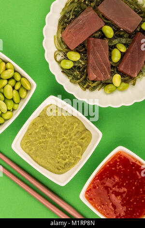 Im japanischen Stil rohen Thunfisch Sashimi auf einem Bett von eingelegtem Algen mit Edamame Bohnen vor einem grünen Hintergrund Stockfoto