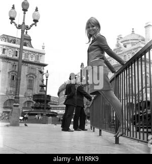 Ein Modell stellt in einem zweiteiligen Rock und Jacke im Freien im Londoner Piccadillyby zwei Polizisten patrouillieren in ca. 1968 tragen eine bunte mini-kleid. Foto von Tony Henshaw Stockfoto