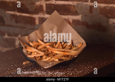 Golden Brown französischen Freunde mit Salz bestreut auf einem hölzernen Tisch gegen die Wand. Stockfoto