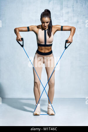 Fitness Mädchen führt Übungen mit Widerstand Band. Foto von Fitness model Workout auf grauem Hintergrund. Kraft und Motivation Stockfoto