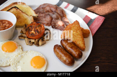 Traditionelles Englisches Frühstück serviert und bereit mit Spiegelei zu essen Würstchen, Pilze, Speck, Bohnen, Toast und gekochten Tomaten Stockfoto