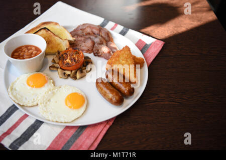 Traditionelles Englisches Frühstück serviert und bereit mit Spiegelei zu essen Würstchen, Pilze, Speck, Bohnen, Toast und gekochten Tomaten Stockfoto