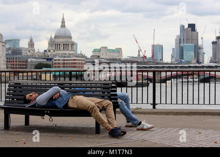 London, Großbritannien - 24 August 2017: Zwei junge Männer in schöne Kleidung und Sonnenbrillen lehnen Sie sich auf einer Bank vor der Skyline von London Stockfoto