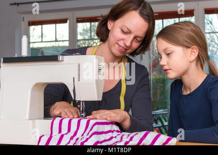 Mutter lehrt ihre 8 Jahre alte Tochter wie eine gestreifte Textilien mit einer Nähmaschine zu nähen. Stockfoto