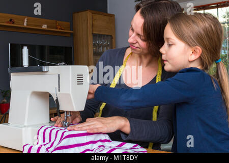 Mutter lehrt ihre 8 Jahre alte Tochter wie eine gestreifte fabics mit einer Nähmaschine zu nähen. Stockfoto