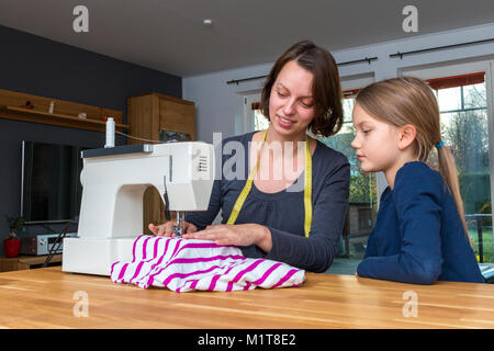 Mutter lehrt ihre 8 Jahre alte Tochter wie eine gestreifte fabics mit einer Nähmaschine zu nähen. Stockfoto