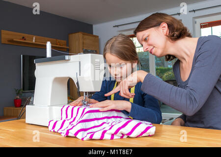 Mutter lehrt ihre 8 Jahre alte Tochter wie eine gestreifte fabics mit einer Nähmaschine zu nähen. Stockfoto