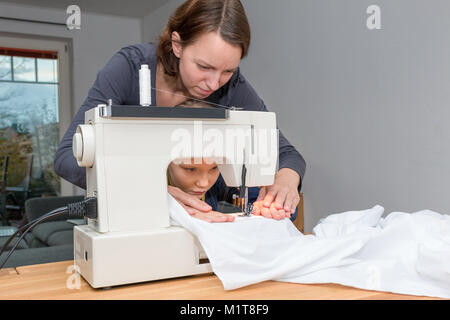 Mutter lehrt ihre 8 Jahre alte Tochter wie eine weiße fabics mit einer Nähmaschine zu nähen. Stockfoto