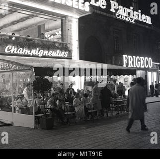 1950, historische, cafe Gesellschaft.... am Abend - Zeit in Paris und die Pariser genießen Sie ein Getränk und Gespräch in ein open Air Cafe Terrasse auf dem Bürgersteig einer gepflasterten Straße in der Nähe der Champs-Elysées. Stockfoto