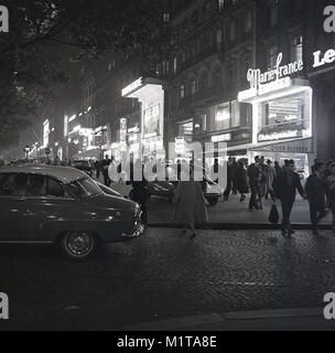 In den 1950er Jahren, historisch, abends in Paris und einer belebten Avenue des Champs-Elysees wird durch die Neonlichter der Einzelhandelsgeschäfte und Werbeschilder beleuchtet. Hier kann man Pariser auf der Avenue spazieren sehen, französische Autos der damaligen Zeit und das Marie France-Geschäft und das Normandie-Kino in der 116 Avenue des Champs-Elysees, das 1937 eröffnet wurde. Stockfoto